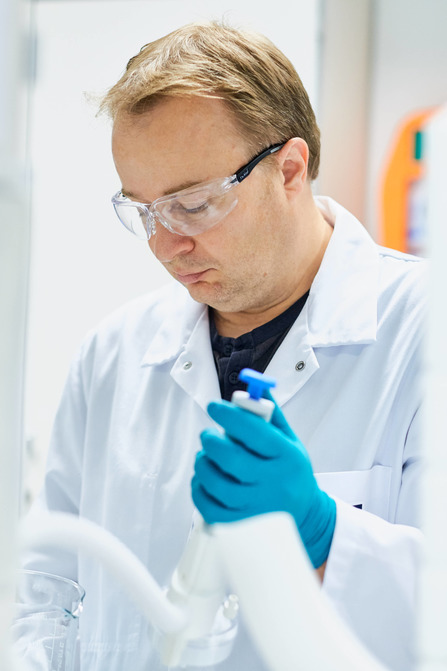 Scientist in white lab coat and blue gloves holds research tool