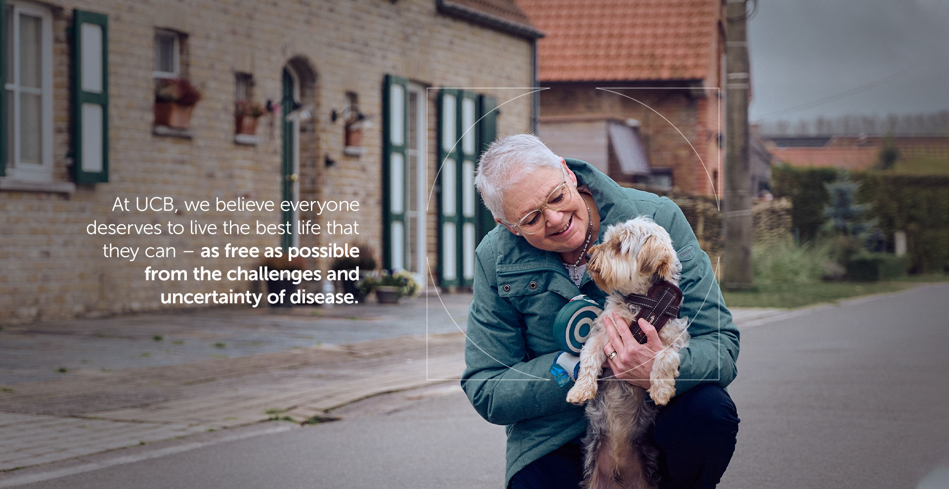 Patient in winter coat holding a small dog and smiling with overlaying text on UCB's mission to help patients live the best lives they can 